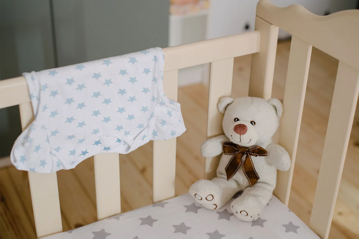 crib with teddy bear and clothing in baby nursery