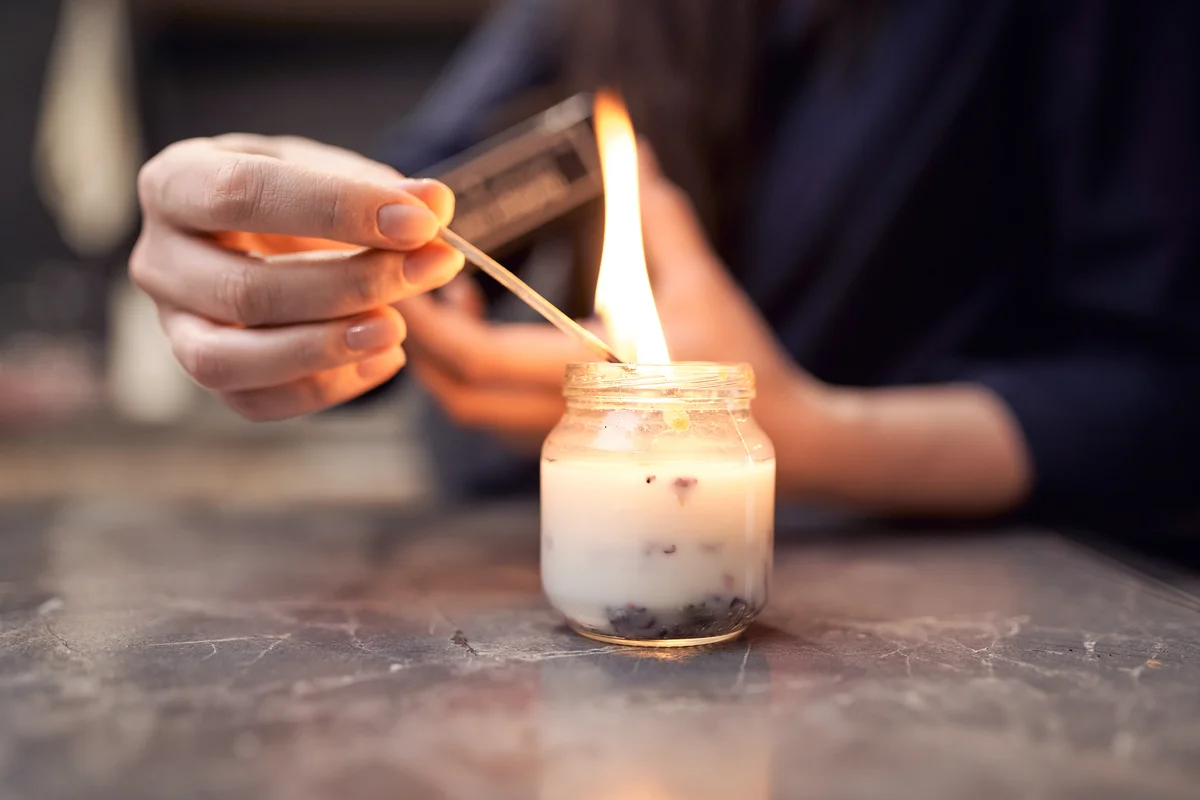 Woman with burning match lighting candle in glass jar