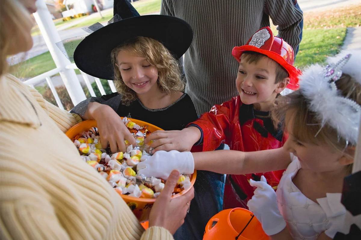 passing out Halloween candy to trick or treaters in costumes
