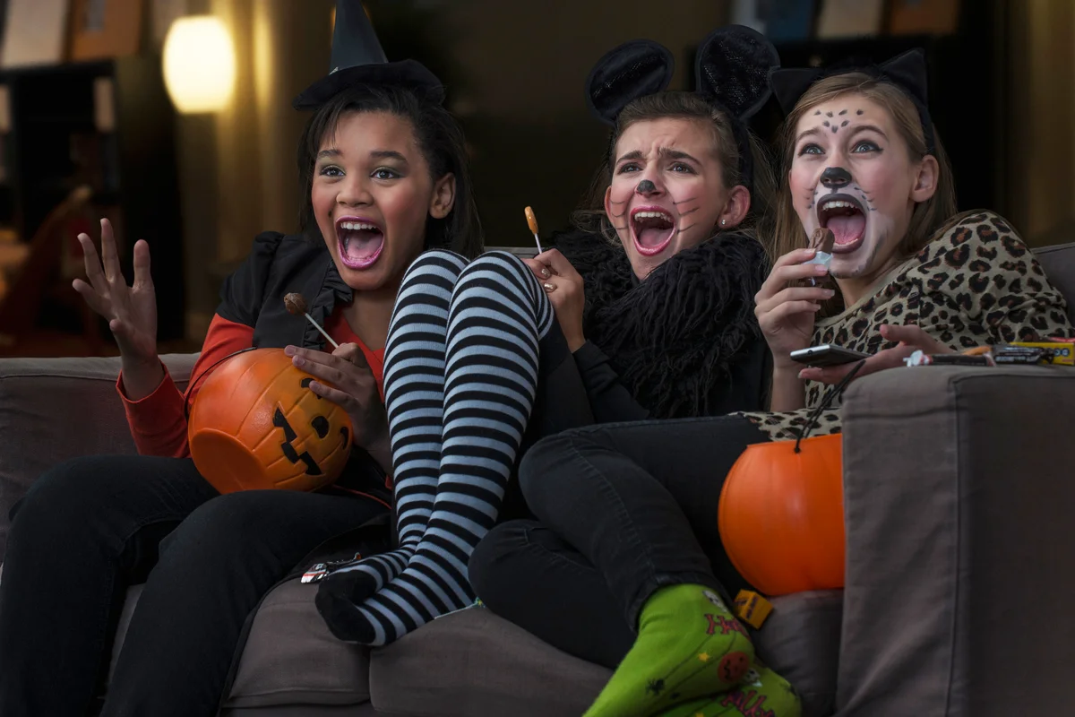Girls in costumes watching scary movie together on Halloween