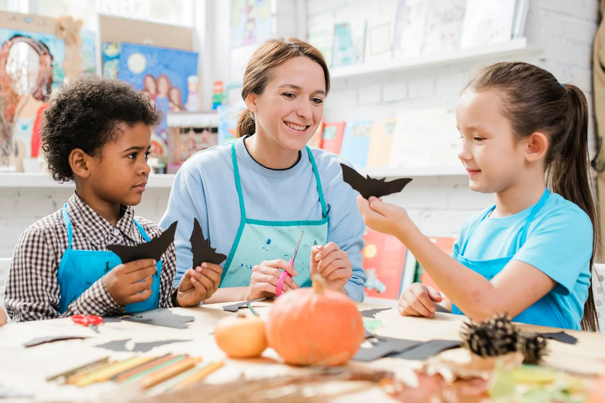 Diligent schoolkids making halloween toys and showing them to happy teacher