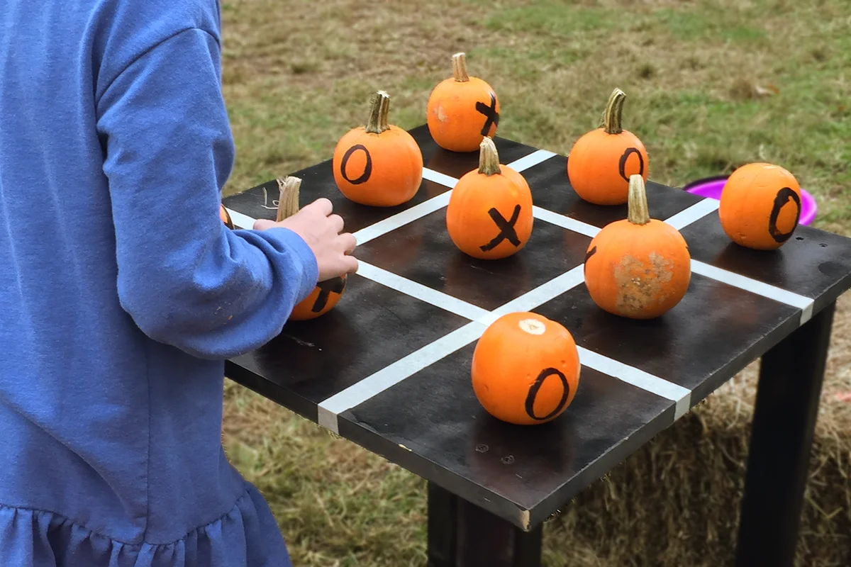 A person playing A Pumpkin Tic-Tac-Toe game adorned with bales of hay on a grass field