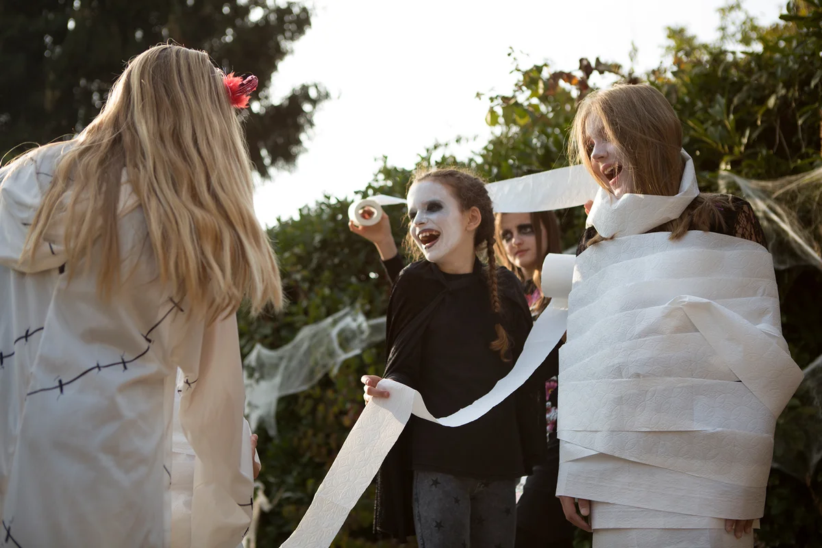 Group of older children playing 'wrap the mummy' Halloween game with toilet rolls