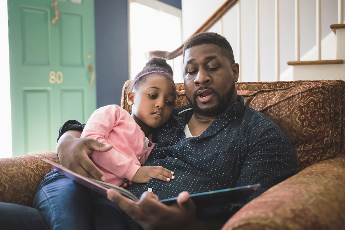 Father and daughter reading book in living room at home