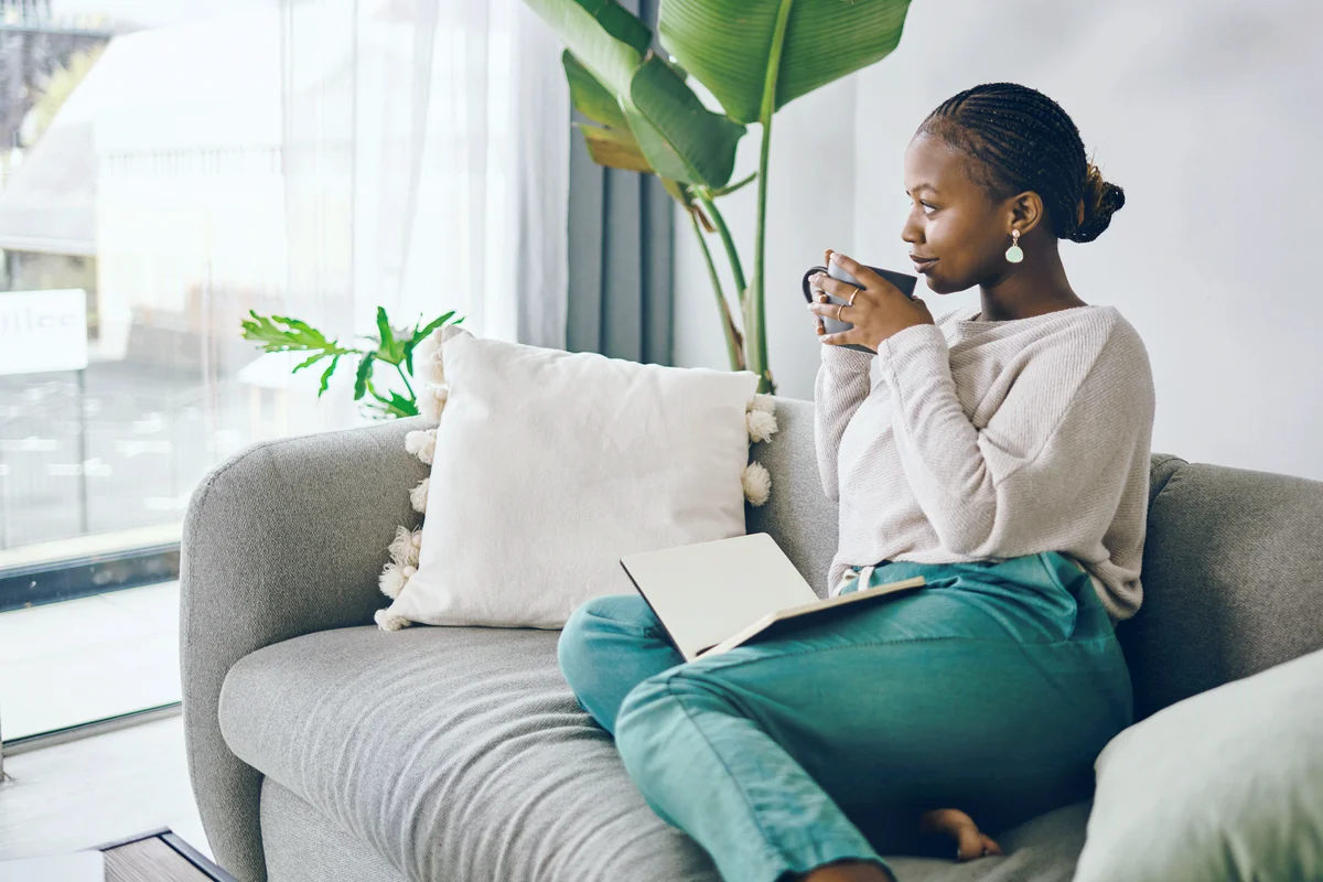 Young woman writing in her journal and relaxing on the couch at home