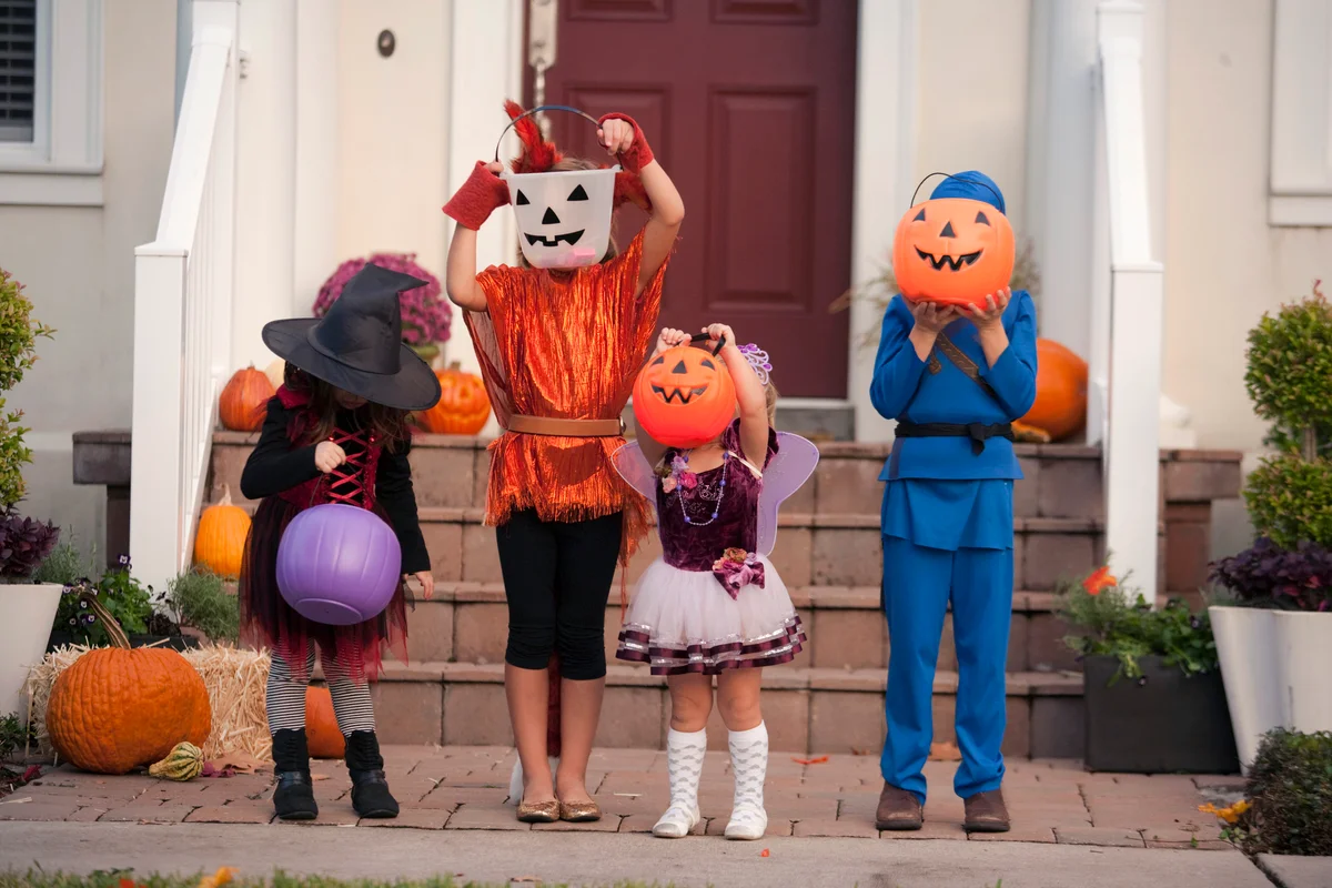 Children covering face with Jack O Lantern bucket in front of house
