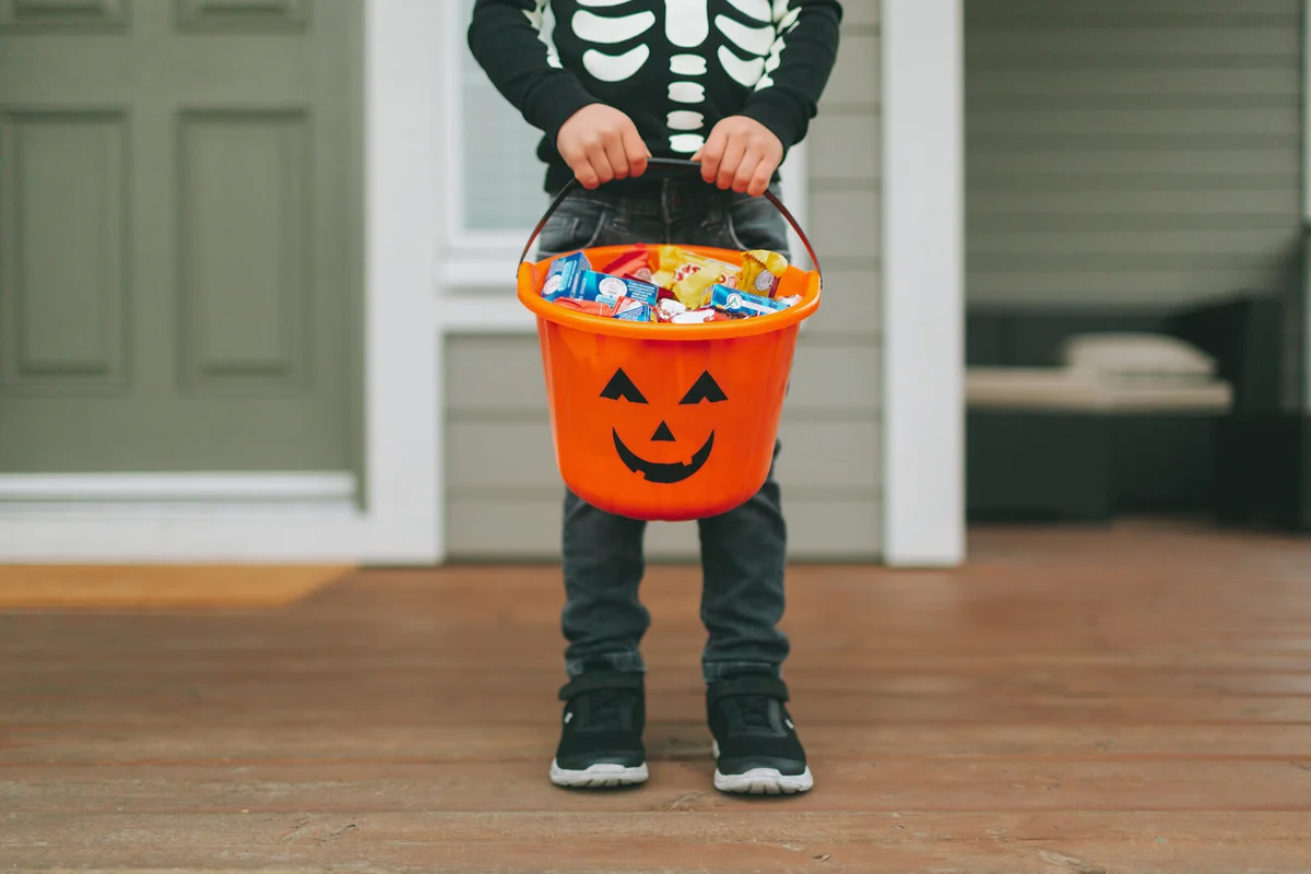 Boy With Sweet Food In Bucket Standing At Home During Halloween
