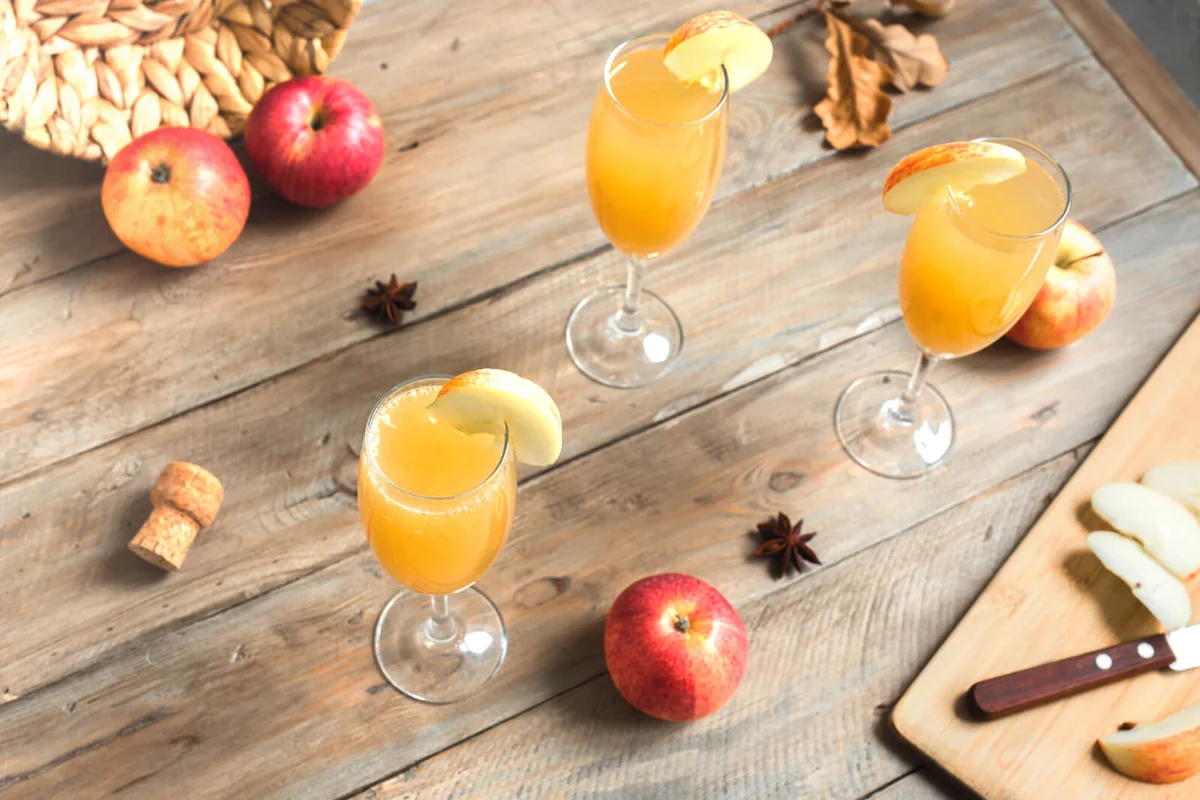 Apple Mimosa Cocktail in tall glasses and organic apples on wooden