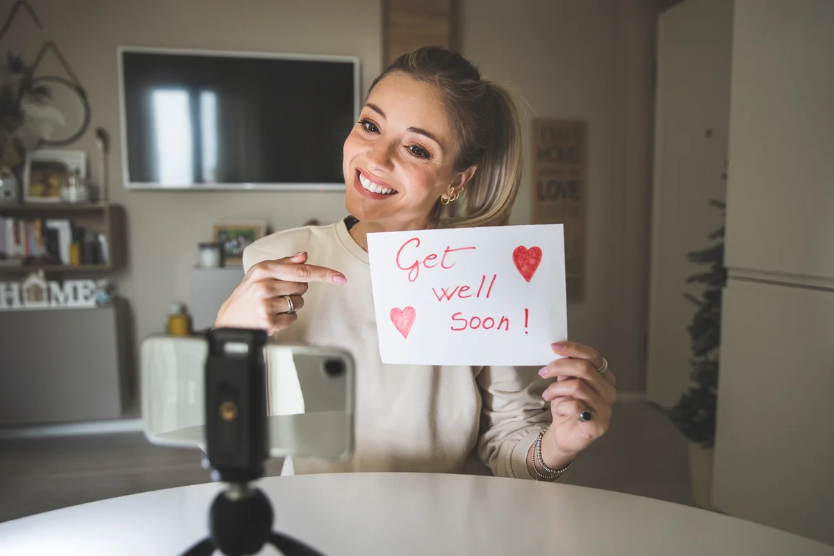 Woman in video call with a friend holding a message to get well soon