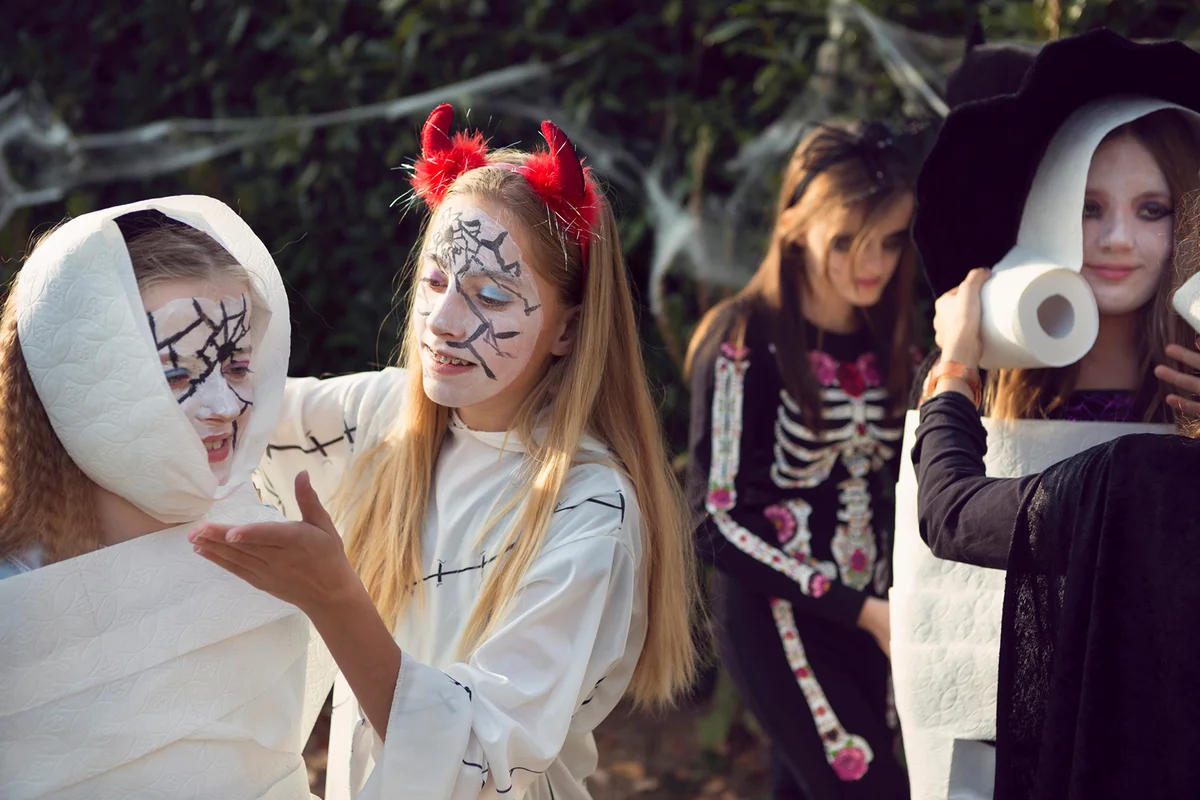 Group of older children playing 'wrap the mummy' Halloween game with toilet rolls