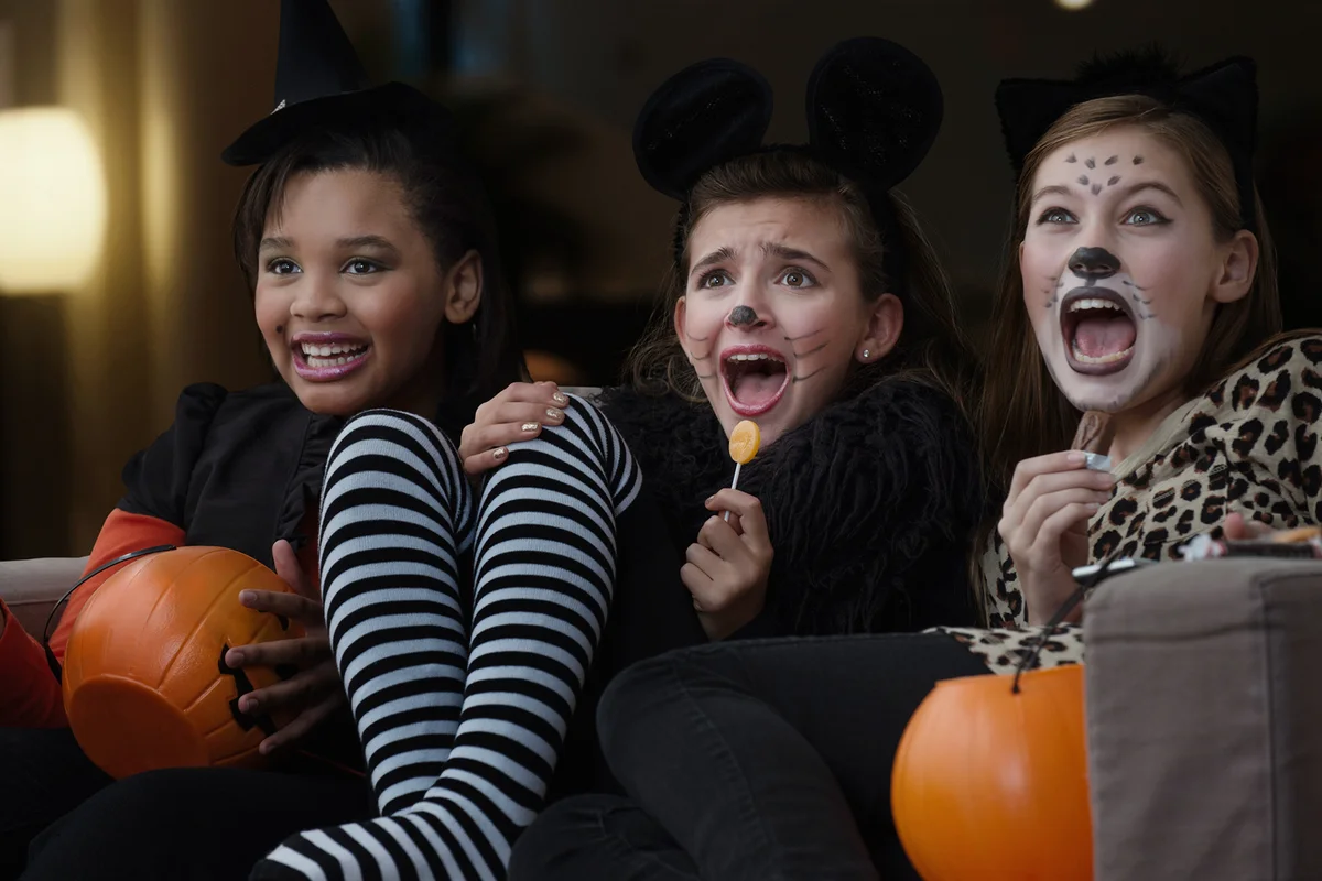 Girls in costumes watching scary movie together on Halloween