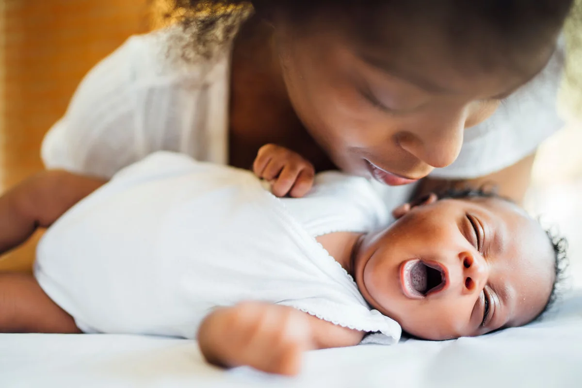 mother looking at cute newborn daughter yawning while lying on bed