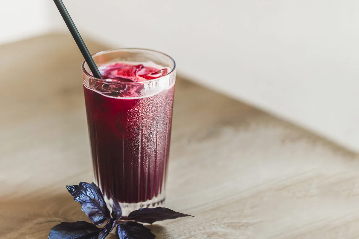 Glass of cold red berry lemonade with fresh basil on table