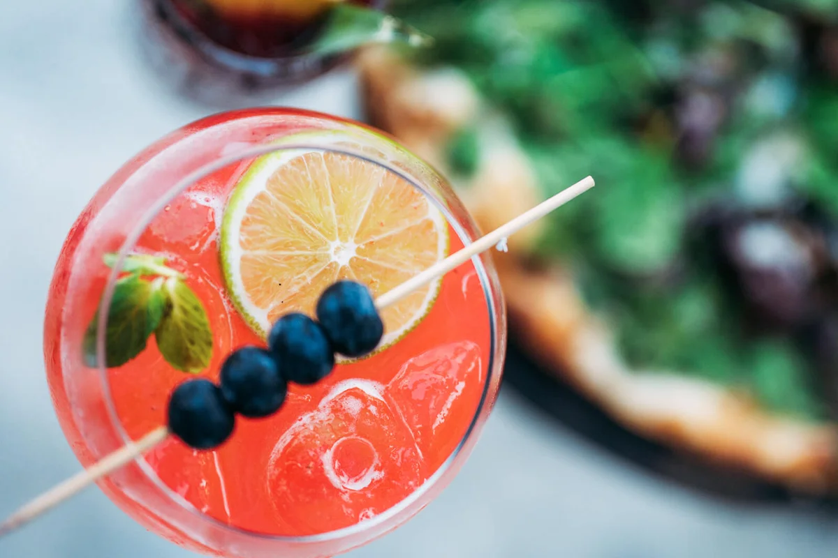 Directly above the red cocktail next to the pizza