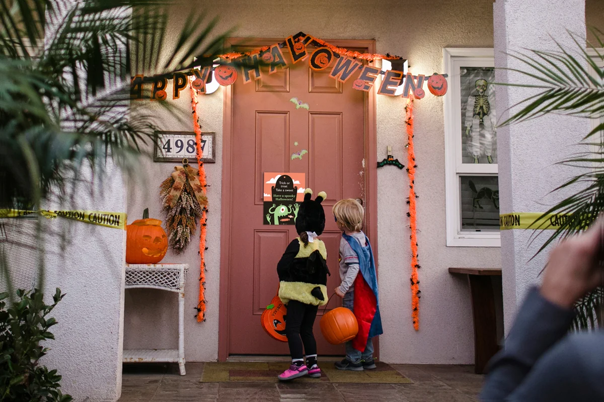 Rear view of siblings wearing costumes while trick or treating on porch during Halloween