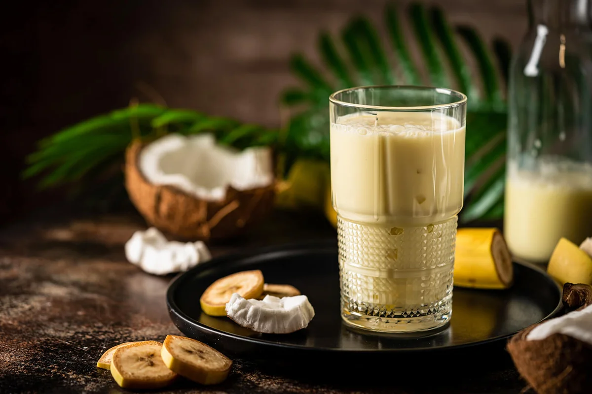 banana cocktail with coconut milk in a glass on dark background with palm leaves