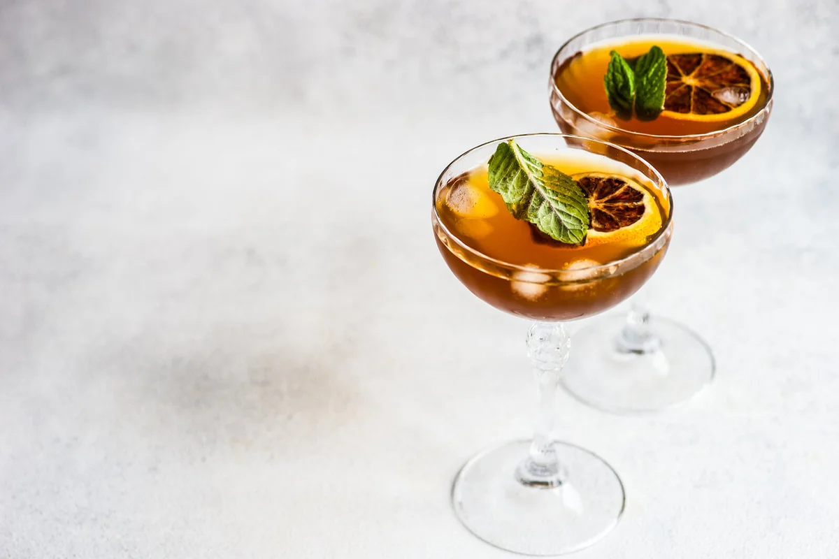 two cocktails with slices of orange and fresh mint