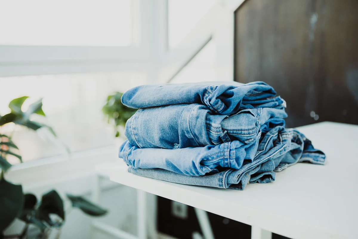 Folded pile of jeans on white wood table at home