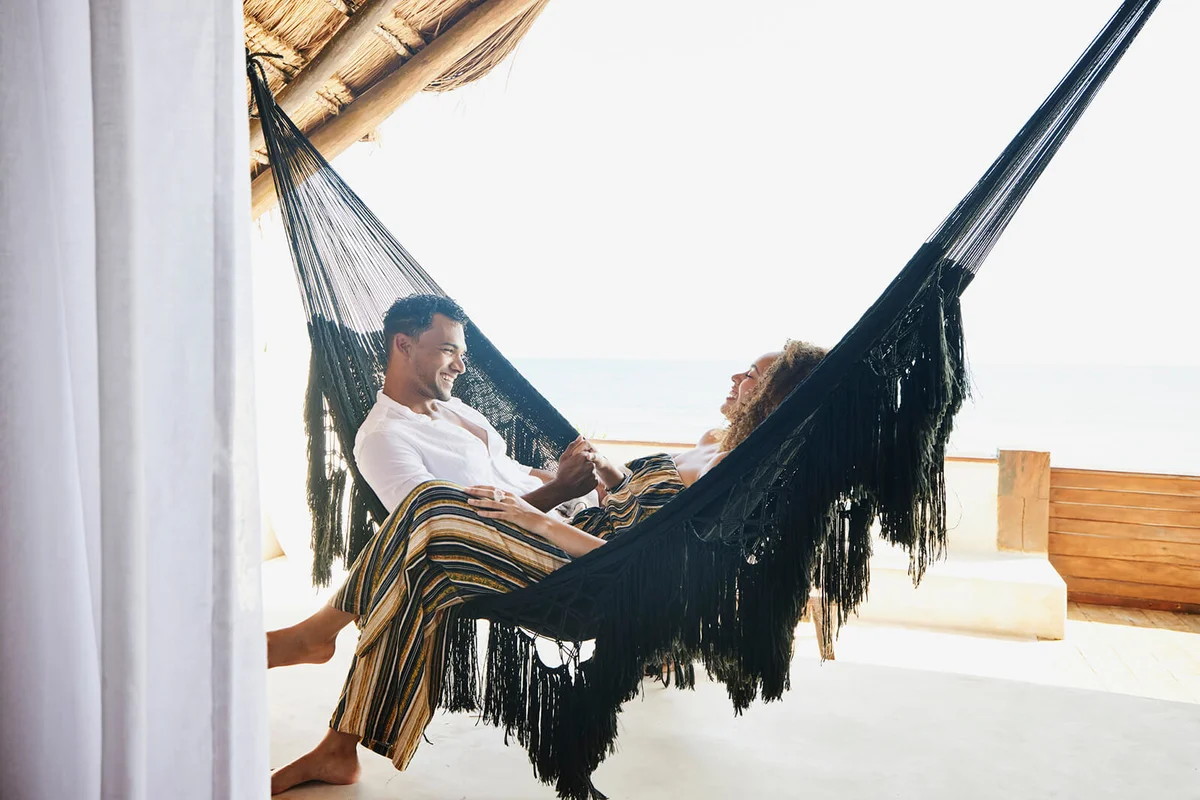 smiling couple holding hands while sitting in hammock