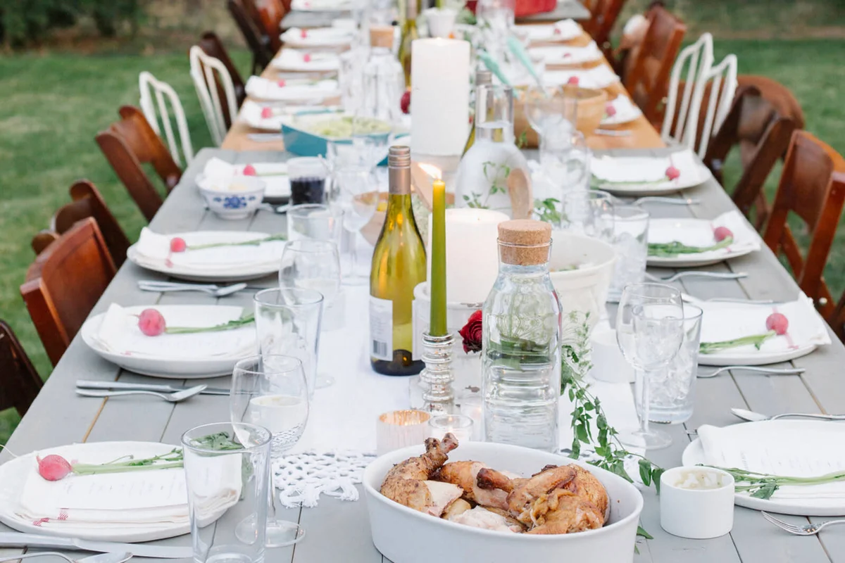 Long table set with plates and glasses, food and drink in a garden