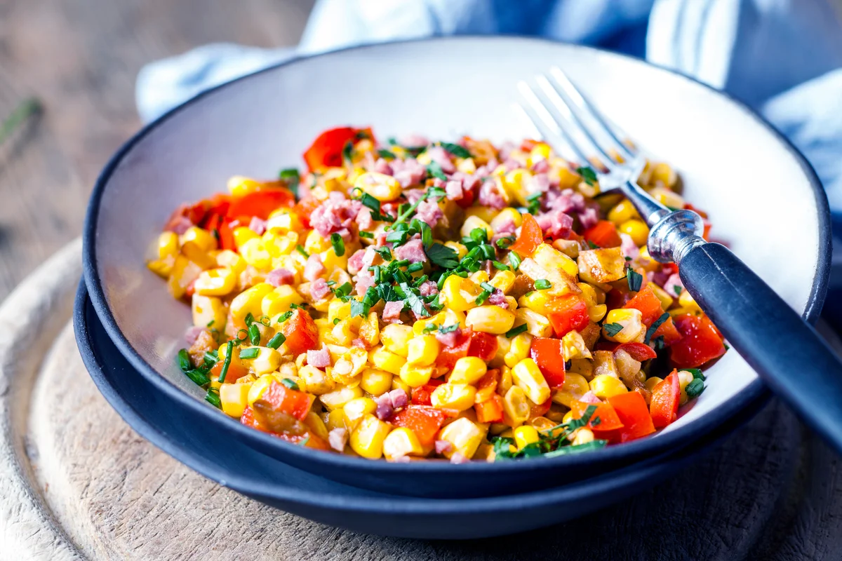 Bowl of warm corn salad with bell pepper, potatoes and diced ham