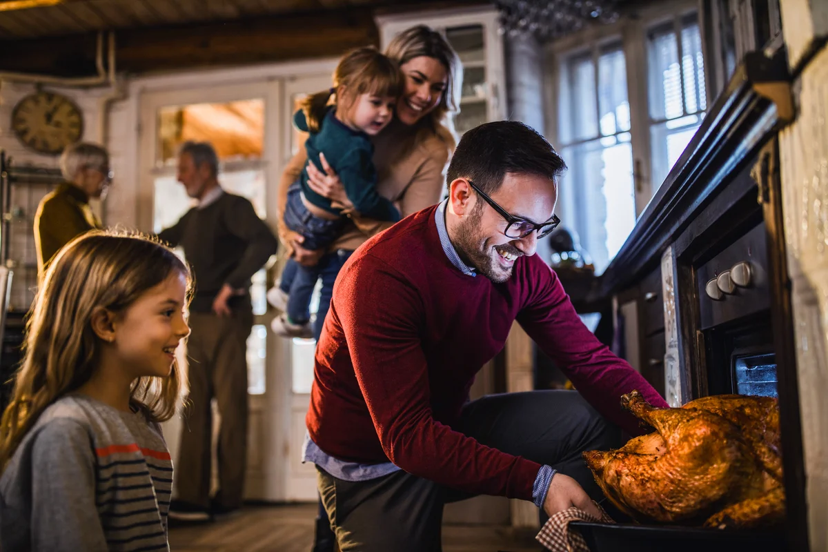 Young happy man taking out baked Thanksgiving turkey from the oven