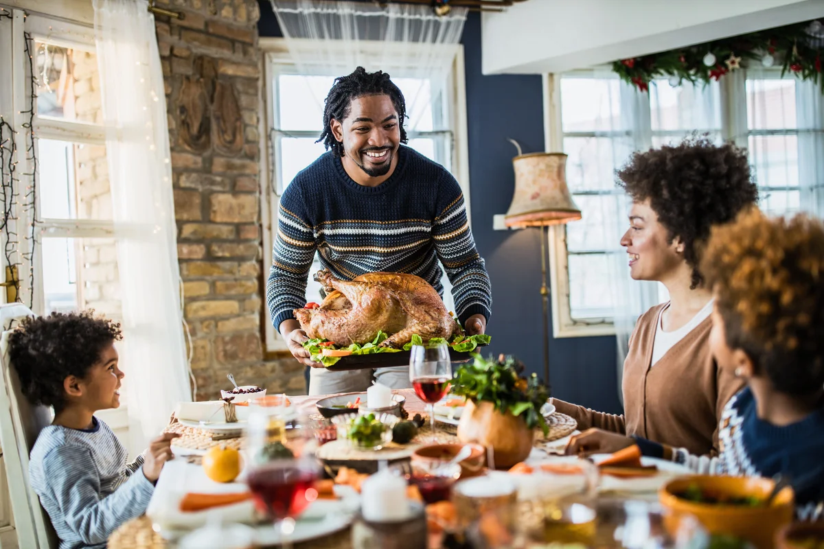 Happy father bringing Thanksgiving turkey to the table