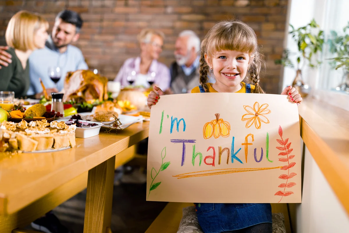 Happy girl holding 'I'm thankful' sign during Thanksgiving meal with her parents and grandparents