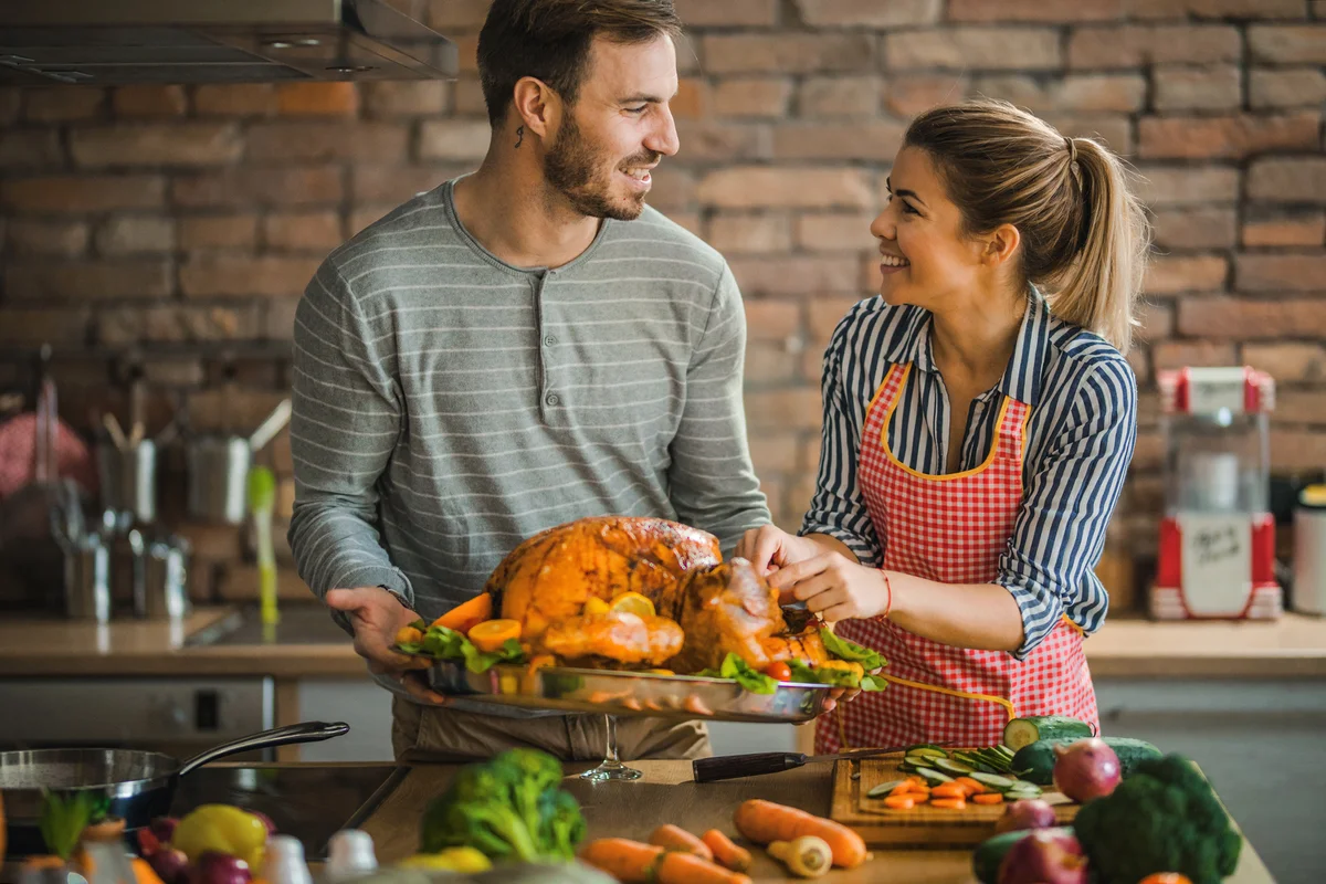 Happy couple talking while decorating turkey on Thanksgiving day