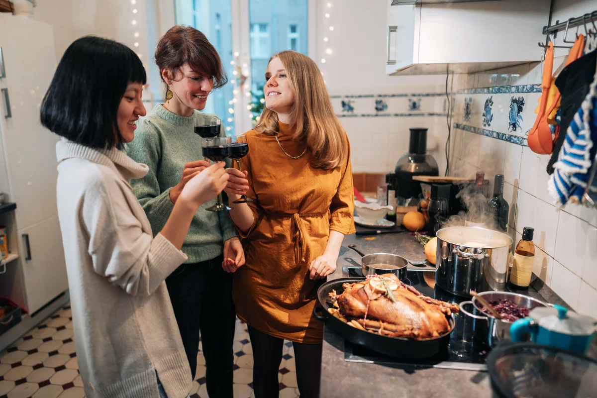 Three women drinking wine while preparing thanksgiving dinner at home