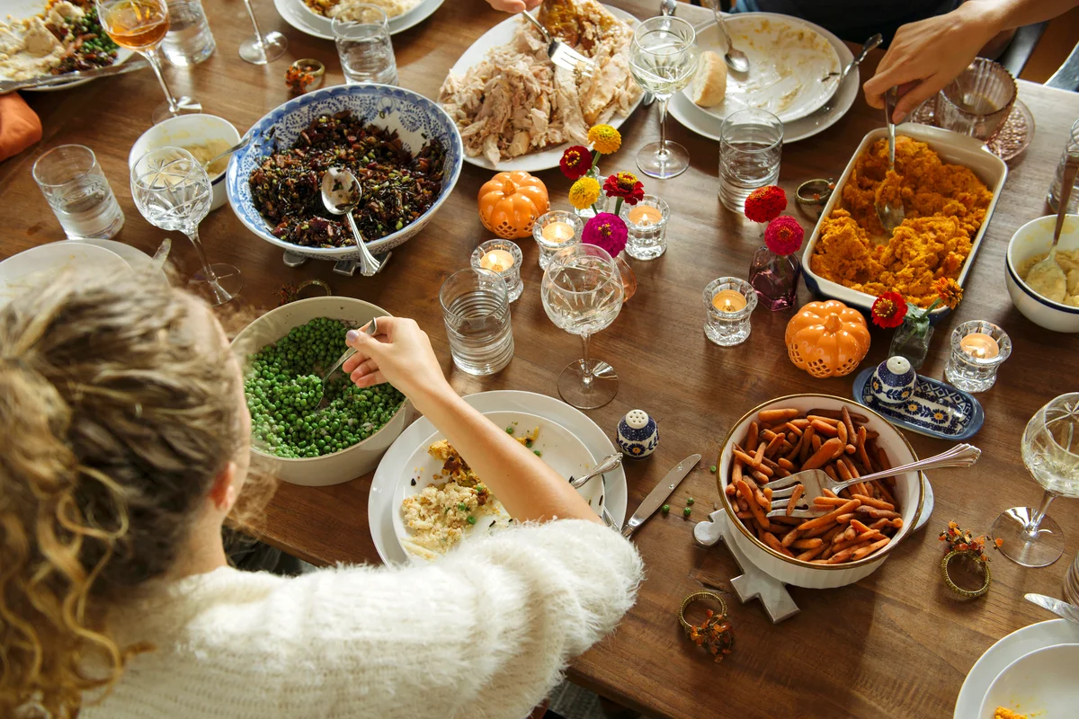 Young woman having food while sitting at dining table during Friendsgiving