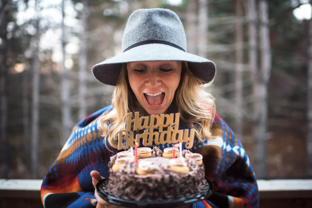 Cheerful woman holding birthday cake while standing outdoors