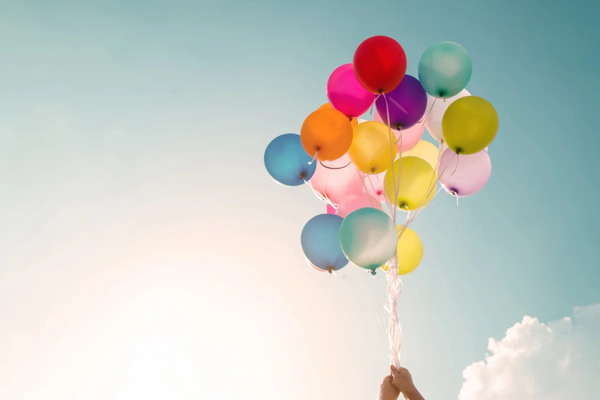 Low Angle View Of Hand Holding Balloons Against Sky