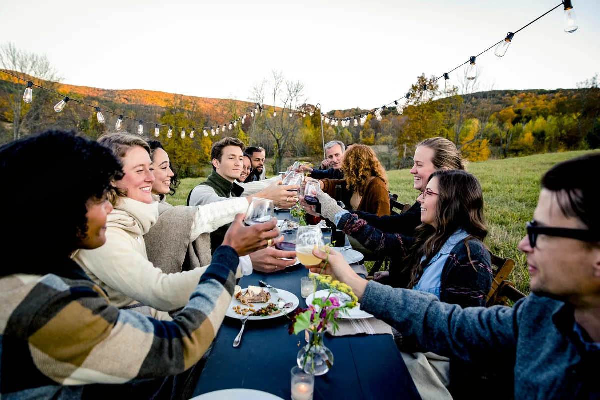 Group of friends toasting at outdoor dinner party in field