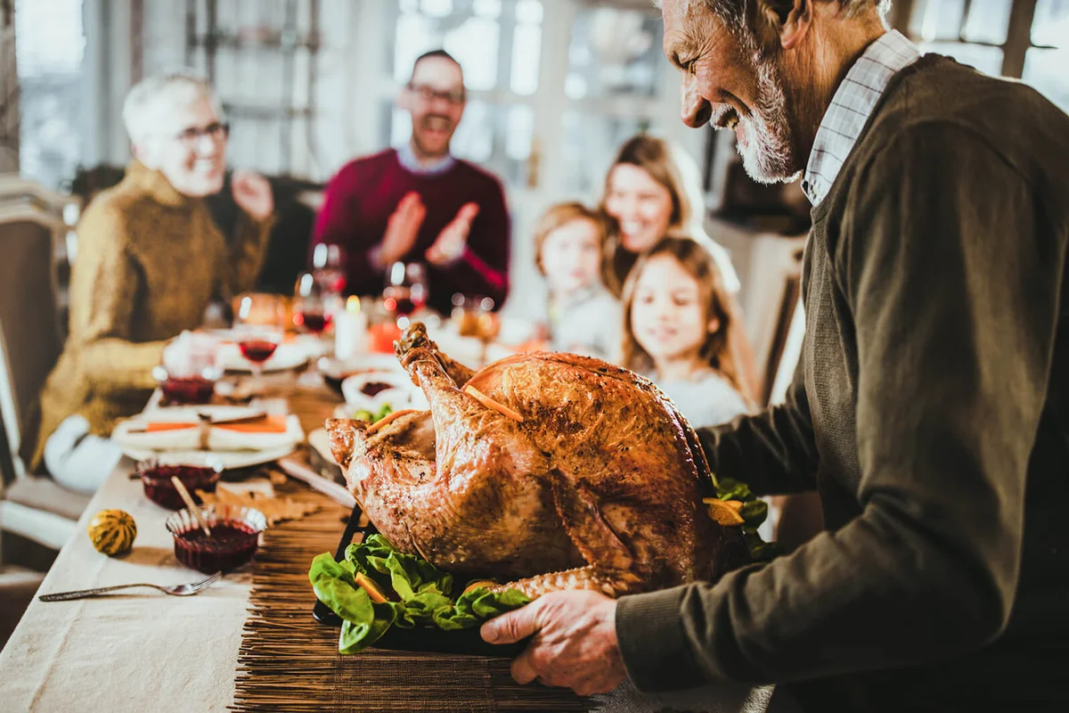 Happy senior man bringing Thanksgiving turkey to the table for his family's lunch
