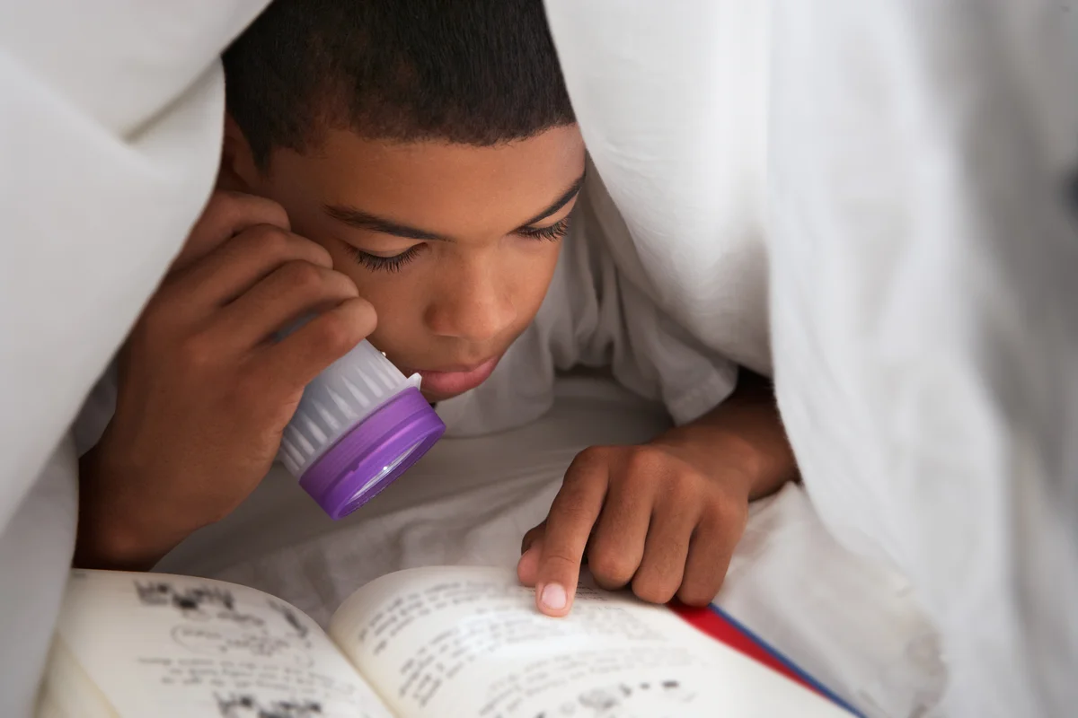 Boy Reading Book Under Blanket