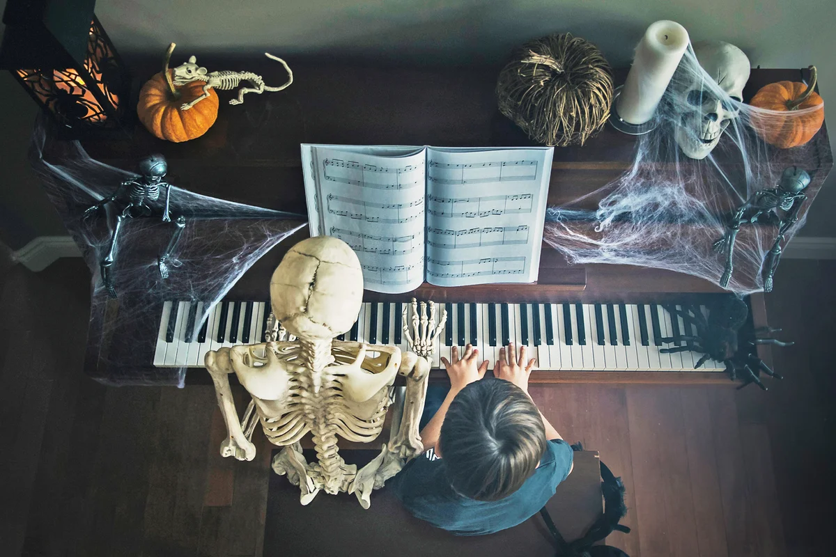 Boy playing piano sitting by skeleton Halloween