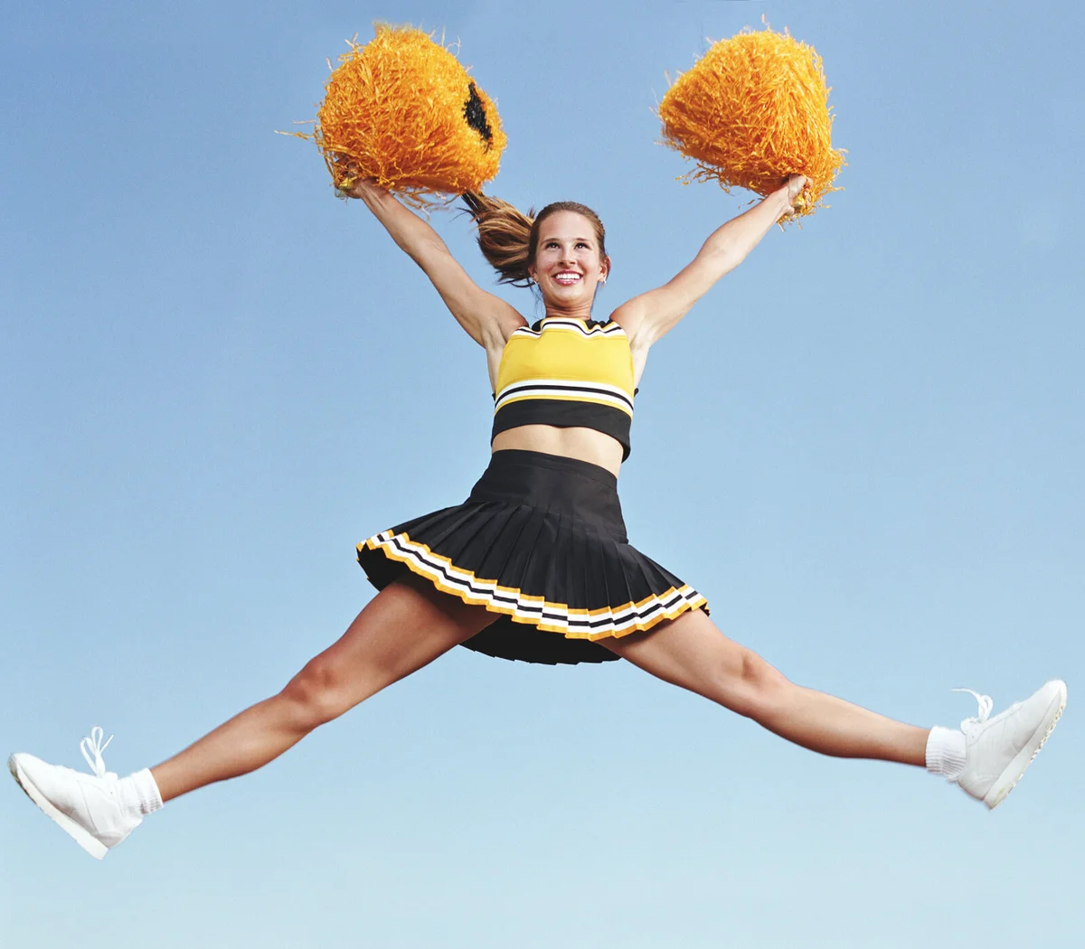 Cheerleader jumping with pompoms in mid air -