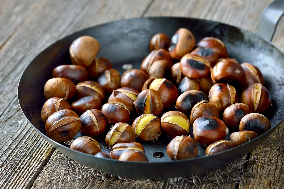 Roasted chestnuts served in a special perforated chestnut pan on an old wooden table