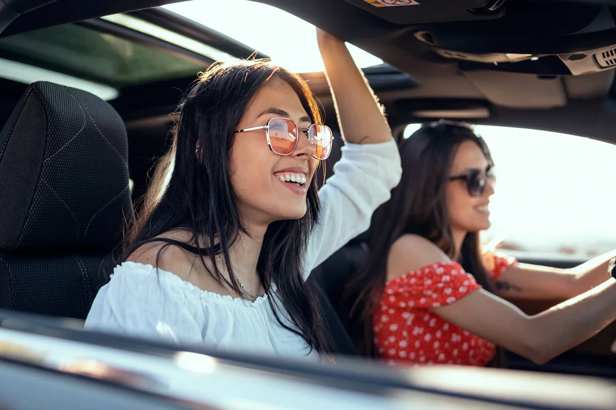 Pretty young women singing while driving a car on road trip on beautiful summer day