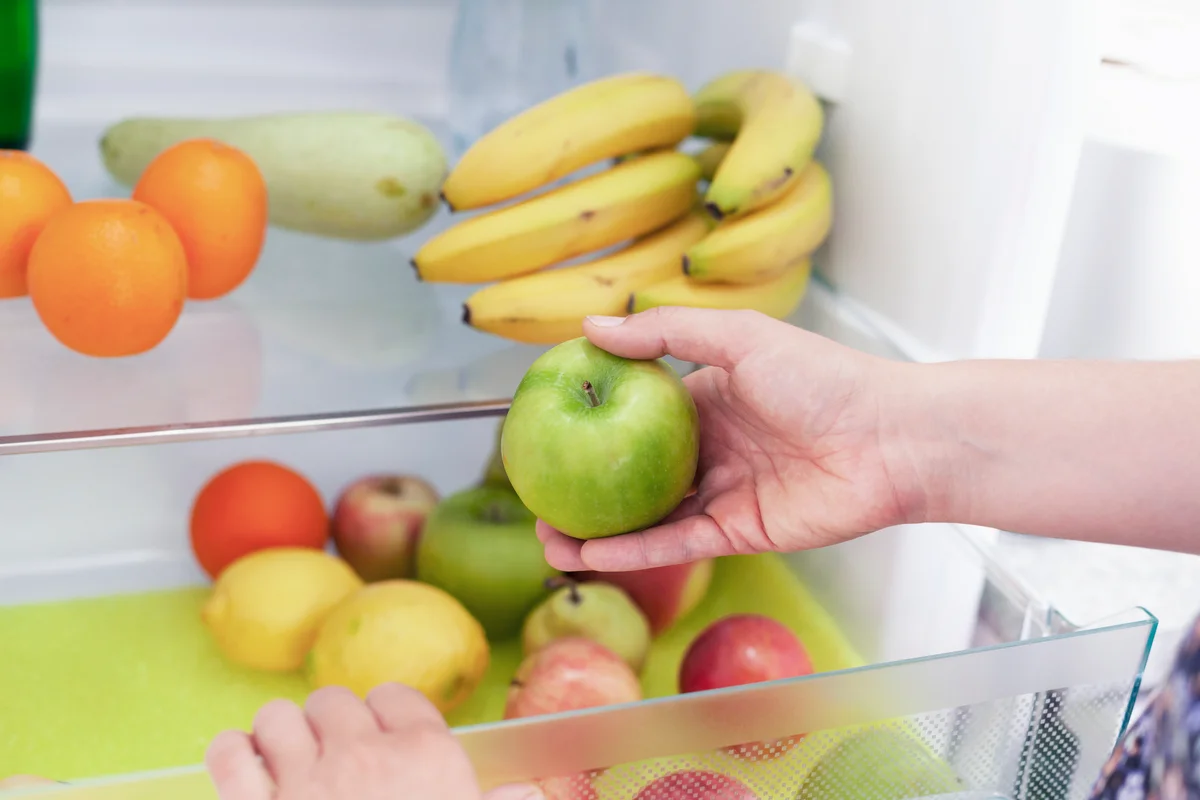 Woman storing apples in fridge