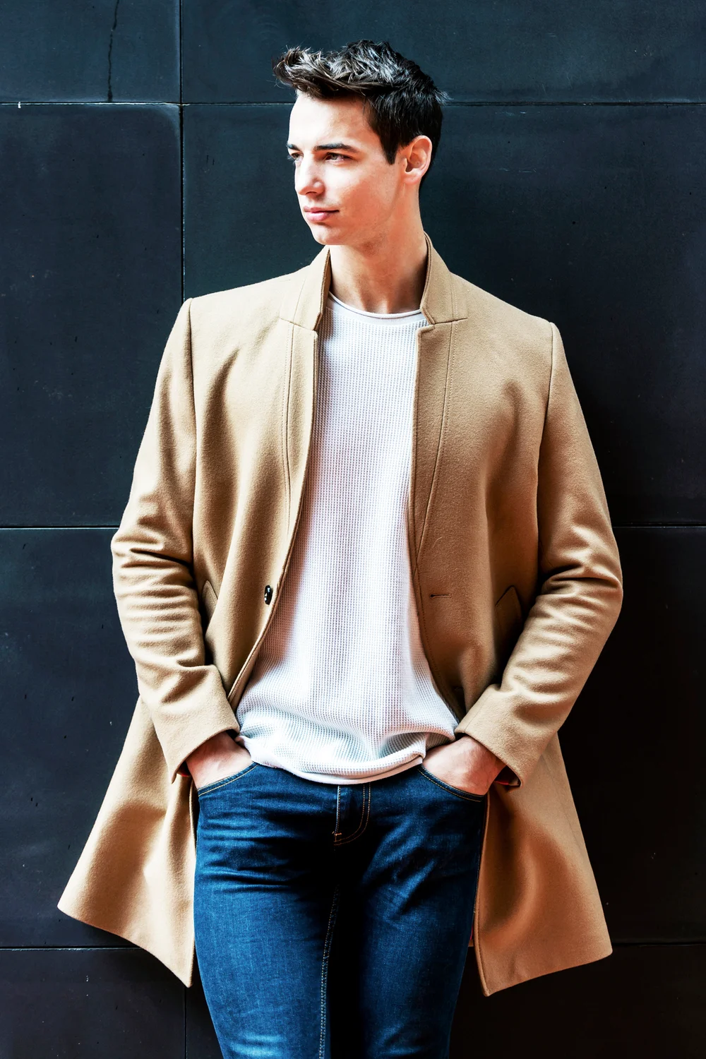 Young man in camel coat standing against wall