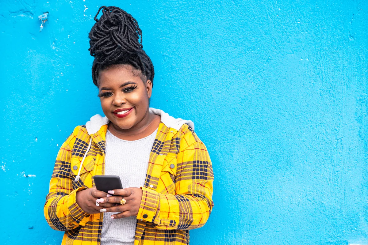 Woman in yellow flannel jacket using smart phone on a blue background