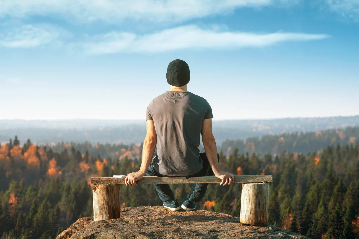 Man sits alone on a lookout point above the forest