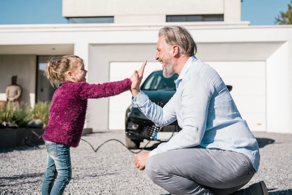Happy girl giving high five to father in front of car on sunny day