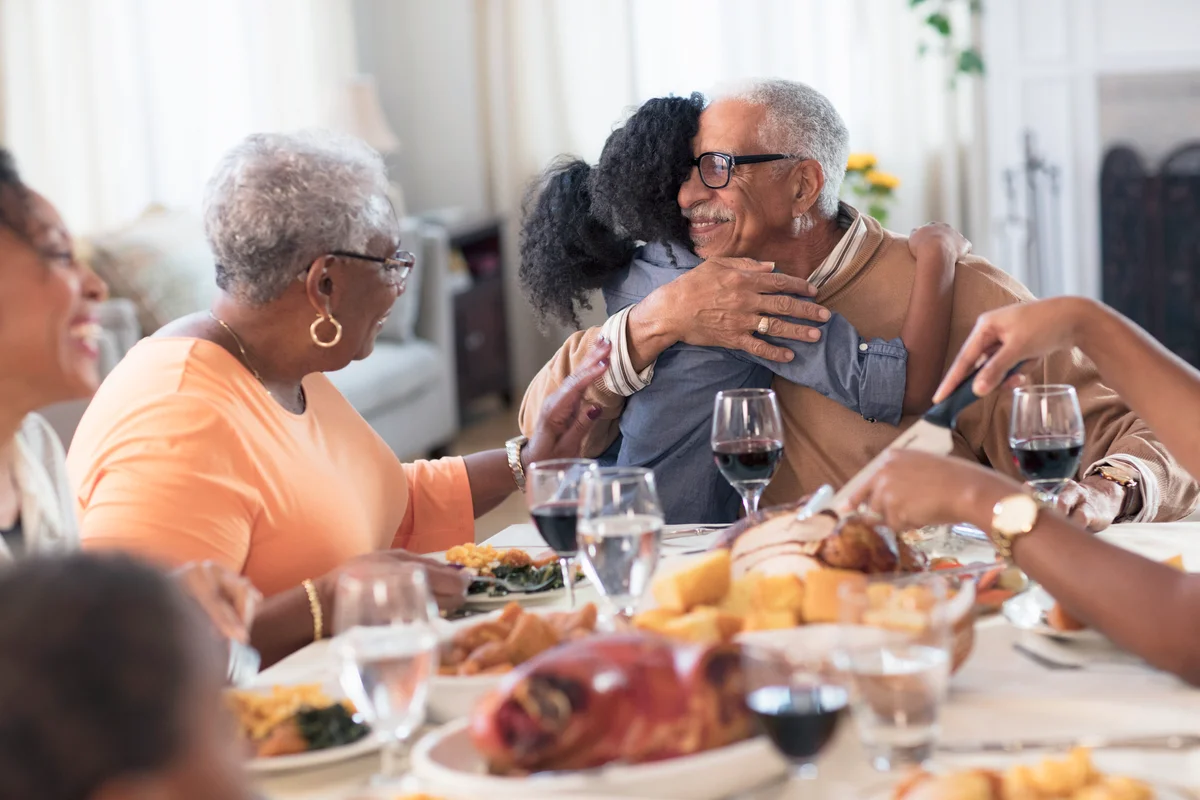 Grandfather hugging granddaughter in dinning room at Thanksgiving