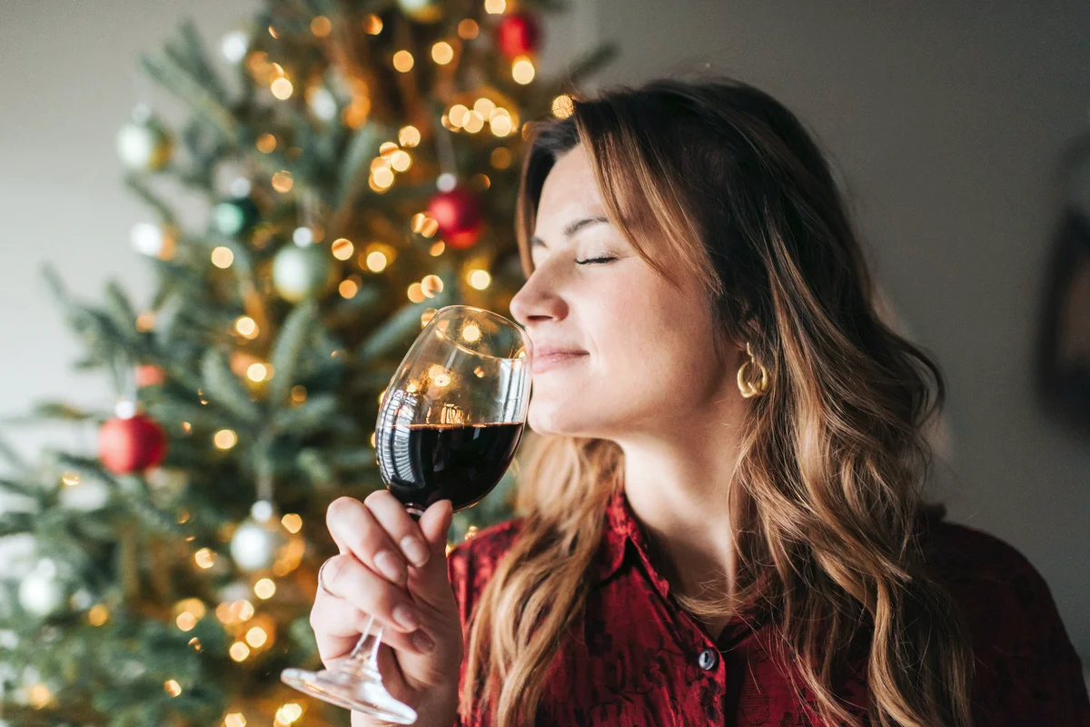 Woman smelling glass of wine beside decorated Christmas tree