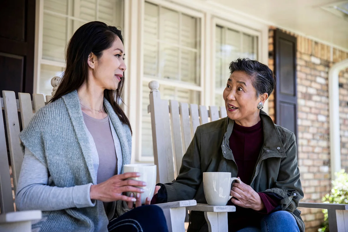 Senior mother and adult daughter having coffee on front porch