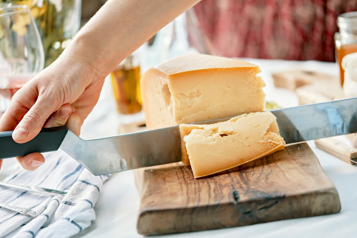 Hands cutting cheese on wood charcuterie board