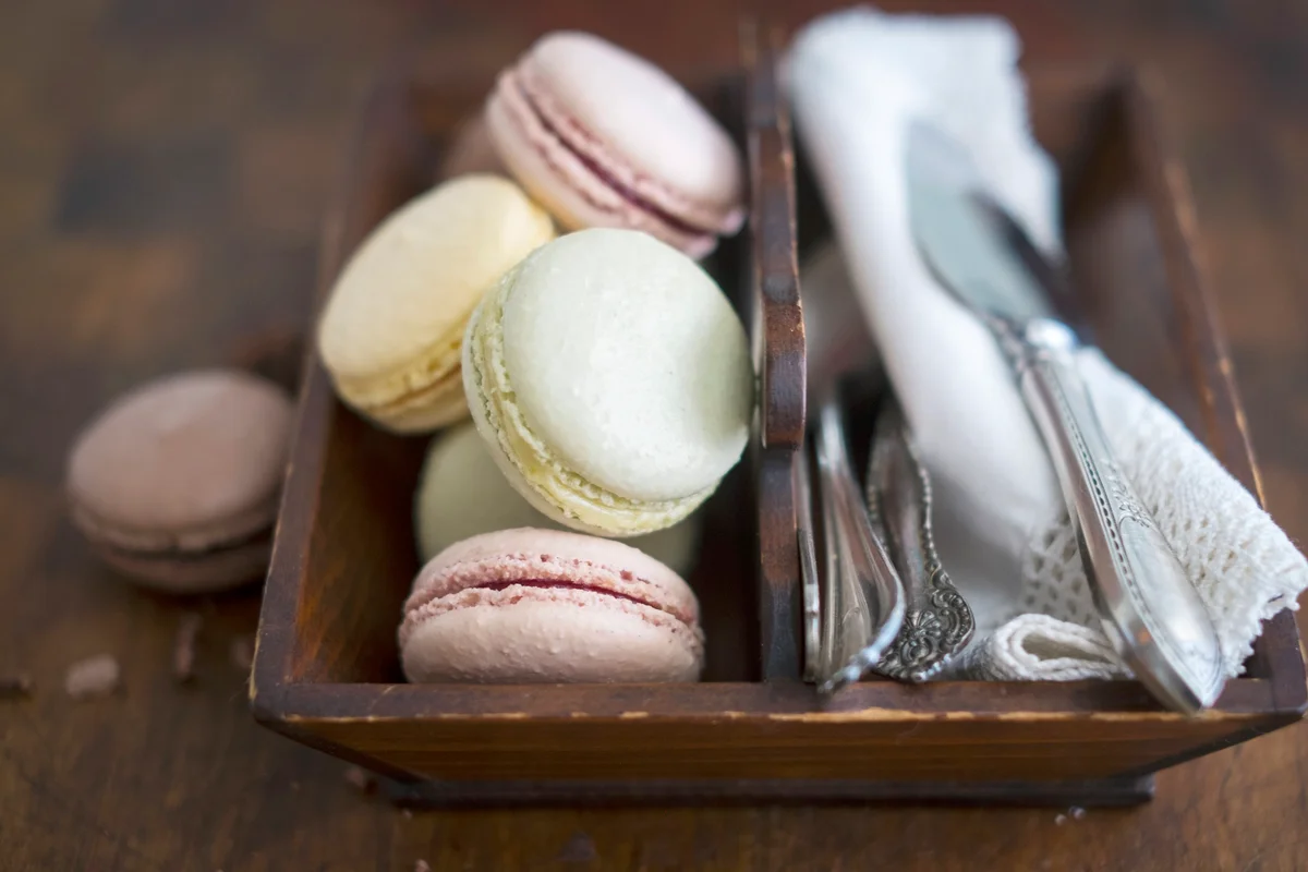 Various colourful macarons with cutlery and napkins in a wooden box